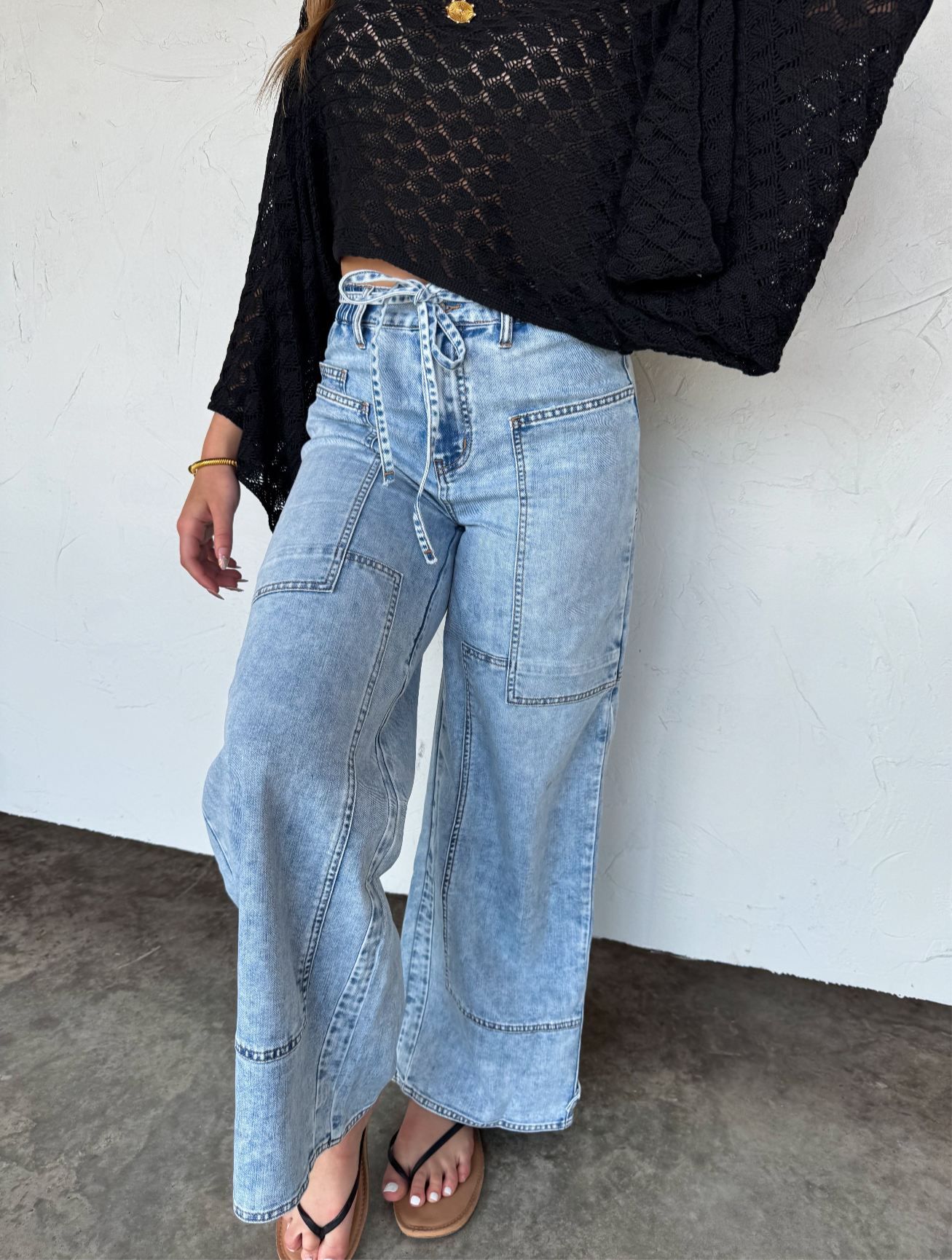 Person wearing light blue wide-leg jeans and a black top against a white wall.